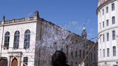 Dresden, Almanya - 11 Nisan 2025: Bir sokak sanatçısı büyük bir değnekle Almanya 'nın Dresden kentinde şehir binaları ile çok sayıda sabun köpüğü yapıyor. Seyahat ve eğlence videoları için ideal.