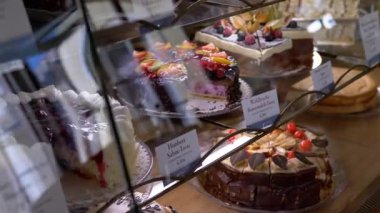 Meyve ve kremayla süslenmiş çeşitli kekler bir kafe vitrininde sergileniyor. Yemek, fırın ve kafe promosyonları için mükemmel..