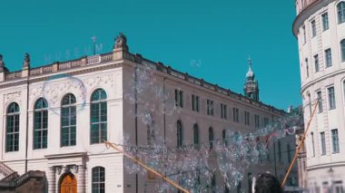 Dresden, Almanya - 11 Nisan 2025: Yanardöner sabun köpükleri deniz mavisi gökyüzüne ve şehir binalarına doğru tembelce sürükleniyor, rüya gibi ve kaprisli bir atmosfer yaratıyor. Fantezi, seyahat ya da eğlenceli video için mükemmel