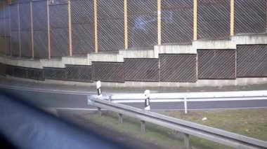 Otoyol kıvrımında hareket eden bir aracın ahşap ses bariyerinin yakın görüntüsü. Ulaşım, altyapı ve kentsel çevre projeleri için ideal.