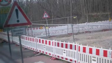 Kırmızı ve beyaz bariyerler, uyarı işaretleri ve hareket halindeki bir araçtan görülen yaya geçidi ile çevrili bir inşaat alanı. İnşaat, güvenlik ve şehir geliştirme videoları için elverişli