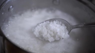Bir kaşık dolusu pirincin kaynayan pirinç lapasından çalındığı yakın çekim. Bu çekim pilavın dokusunu ve pişirme sürecini vurgular..