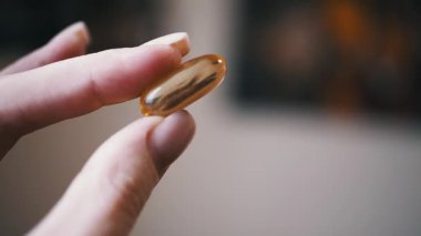 Balık yağı kapsülü, bulanık bir arka planda iki parmak arasında, sağlık ve sağlıkla ilgili projeler için idealdir..