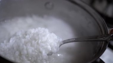 Pirinç lapasının kalın, kremalı kıvamını gösteren, pilavı tencereden kaldıran bir kaşık yakın plan. Yemek blogları ve yemek programları için ideal..