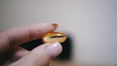 Parmaklar arasında tutulan balık yağı kapsülünün yakın çekim görüntüsü. Sağlık destekleri, beslenme ve sağlıkla ilgili projeler için mükemmel..