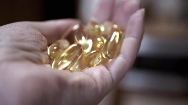 Bir el, günlük takviyelerin önemini vurgulayarak birkaç altın balık yağı kapsülünü nazikçe tutuyor. Sağlık ve sağlık videoları için mükemmel..