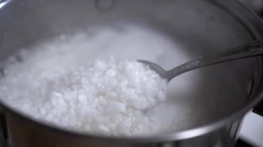 Pirinç lapasından pilav kaldıran bir kaşığın detaylı görüntüsü yumuşak dokuyu ve ışıldayan taneleri vurguluyor. Tarif videoları için mükemmel.