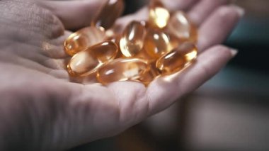 Bir avuç dolusu altın balık yağı kapsülünü tutan bir elin yakınına. Sağlık, sağlık ve ek projeler için ideal.
