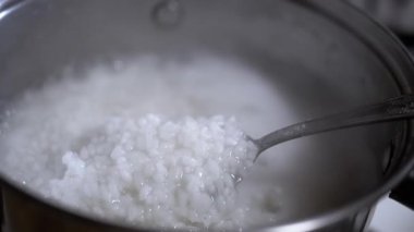 Pirinç lapası metal bir tavada pişirilir. Kaşıkla, lapanın hazır olup olmadığını kontrol et. Sağlıklı yemek pişirmek..