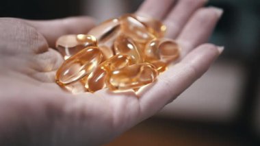 Bir kadın eli, bir avuç balık yağı kapsülünü tutarak, sağlık malzemelerinin önemini gösterir. Sağlık, sağlık ve beslenme projeleri için ideal.