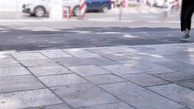 Bir insan şehir kaldırımında yürür, bacaklar ve ayakkabılar görünür. Arka planda bulanık cadde ve yaya trafiği var. Kentsel yaşam tarzı konsepti.