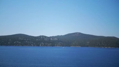 Körfezin sakin mavi suları, adanın yeşil tepeleri ve berrak gökyüzü sakin bir manzara yaratır. Küçük tekneler ufukta belirdi. Barışçıl Karadağ.