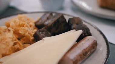 Yağda yumurta, peynir, sosis ve siyah ekmek ile lezzetli ve besleyici bir kahvaltı gösteriliyor. Bir fincan kahve ve hamur işi yemeği tamamlar, rahat bir sabah ortamı yaratır..