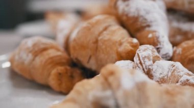 Baştan çıkarıcı, taze pişmiş kruvasan tozları pudra şekerle kaplanmış, altın-kahverengi renklerini ve pul pul dokularını sergiliyorlar. Yemek ve yaşam tarzı içeriği için enfes bir görsel..