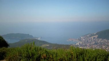 Karadağ 'ın Budva kenti aşağıda, dağlarla Adriyatik Denizi arasında yuva yapmış canlı bir şehir manzarası gözler önüne seriliyor. Bu hava perspektifi kıyı şeridinin, adaların ve kentsel yaşamın güzelliğini yakalar..
