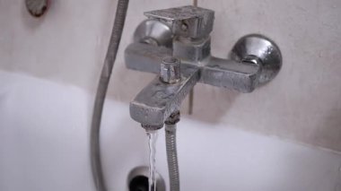 Kirli, paslı bir banyo musluğundan küvete su akıyor. Aşınmış armatür ve fayanslar temizlik ya da onarım ihtiyacını vurguluyor.