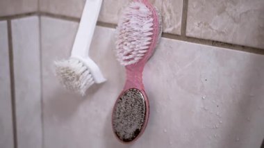 İki iyi kullanılmış fırça, biri beyaz biri pembe, su lekeli bir duş duvarına asılmış, günlük rutin bir duyguyu çağrıştırıyor..