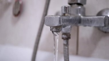 Kirli, paslı bir banyo musluğundan su akıyor. Aletlerin bozulma durumu fayanslı duvara karşı belli oluyor..
