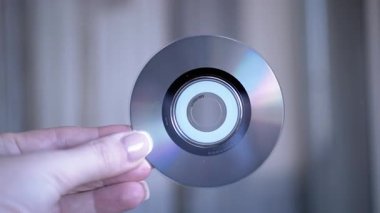 Boş bir CD 'yi tutan bir elin yakın plan görüntüsü, yansıtıcı yüzeyi ve elin detaylarını vurguluyor.