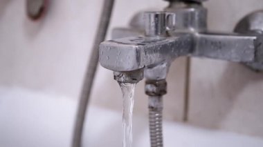 Kirli, paslı bir banyo musluğundan su akar. Aletlerin ve fayansların kötü durumda olması, tadilata ihtiyaç olduğunu gösteriyor..
