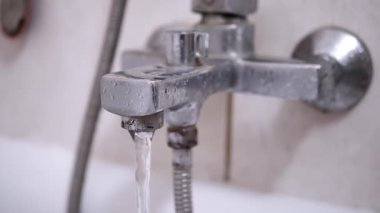 Pis, paslı bir banyo musluğu küvete su dökerek akıyor. Armatür ve fayansların durumu ev geliştirme ihtiyacı olduğunu gösteriyor..