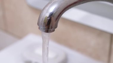 Banyo musluğundan lavaboya su akar. Su akışı bulanık bir zemine karşı temiz ve istikrarlıdır..