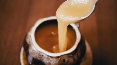 Yapışkan bir altın bal akıntısı kaşıktan tencereye damlıyor. Yemek, yemek ve sağlıklı beslenme videoları için mükemmel..