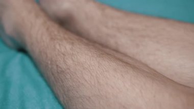 Turkuaz yatak yüzeyinde yatan erkek bacaklarının yakın çekimi. Vücut imajı, sağlık ve yaşam tarzı projeleri için uygundur.