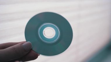 Bir el, şeffaf yüzeyi ve veri kanallarını gösteren parlak bir arkaplan karşısında bir CD tutar. Teknoloji ve veri depolama temaları için ideal.