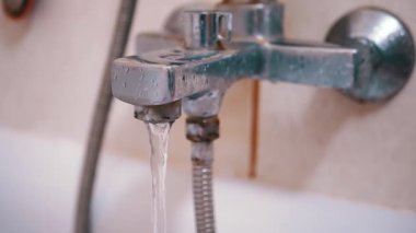 Kirli, paslı bir banyo musluğundan su akıyor. Bozulmuş armatür ve fayanslar banyo tadilatına ihtiyaç olduğunu gösteriyor..