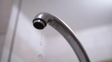 Su damlacıklarının ve metalik yüzeyin vurgulandığı bulanık arka planda, damlayan musluğun yakın plan görüntüsü. Su koruma temaları için uygundur.