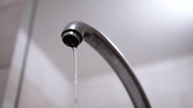 Krom bir musluktan, aşağıdan bakıldığında, yumuşak ve bulanık bir arkaplana doğru sabit bir su akışı akar. Su kullanımı, tesisat ve günlük rutin işler için uygun.