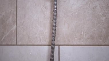 Banyodaki duş başlığından su akıyor, fayanslı duvara çarpıyor. Günlük rutine, hijyene ve ev görüntülerine uygun..