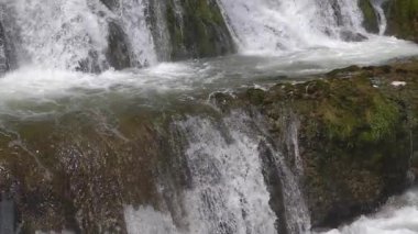 Kayaların üzerinde çağlayan bir şelalenin huzurlu manzarası köpükler ve huzurlu bir ortam yaratıyor. Şelaleden yükselen su ve sisin görüntüsü. Su sıçratıyor. Yakın plan..