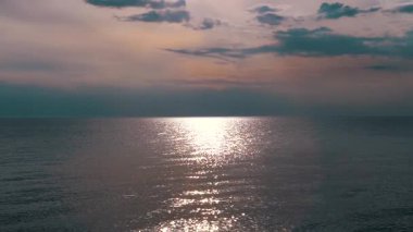 Sahilde sakin bir denizin üzerinde, renkli ve canlı bir gökyüzü tarafından kucaklanan huzurlu bir gün batımı. Huzurlu denizin üzerinde görkemli bir şekilde batan kızıl güneşin nefes kesici görüntüsü, sıcak renkleri yansıtıyor..