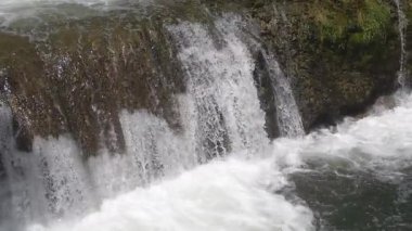 Kayaların üzerinde çağlayan bir şelalenin huzurlu manzarası köpükler ve huzurlu bir ortam yaratıyor. Şelaleden yükselen su ve sisin görüntüsü. Su sıçratıyor. Yakın plan..