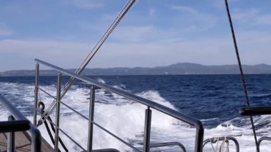 Yakın plan, bir tekne hareket ederken su sıçratan dalgaların görüntüsü. Açık denizde parlak güneşli bir gökyüzünün altında ustalıkla dalgaları geçen bir tekneden manzara. Bir gemiyle deniz yolculuğu. Yavaş çekim.