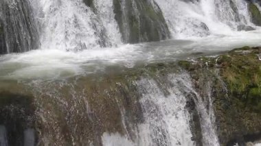 Kayaların üzerinde çağlayan bir şelalenin huzurlu manzarası köpükler ve huzurlu bir ortam yaratıyor. Şelaleden yükselen su ve sisin görüntüsü. Su sıçratıyor. Yakın plan..