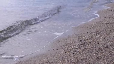 Büyüleyici kıyı şeridi yumuşak dalgaların yumuşak, sıcak bir ışığın altında çakıllı bir plaja hafifçe dokunuşlarını içerir. Kapatın. Bulanık arkaplan.