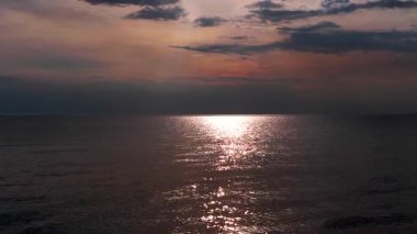 Suya yansıyan sıcak ışınlarla sersemletici deniz batımı. Yumuşak bulutlar, altın, kırmızı güneş ışığı ile aydınlatılır, sakin bir atmosfer yaratır. Güneş ışığı su yüzeyinden yansıyor. Ege Denizi.