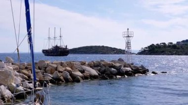 Parlak bir gökyüzünün altındaki engebeli kayalık kıyılarda seyreden görkemli bir yelkenli gemisinin nefes kesici manzarası..