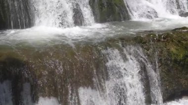 Kayaların üzerinde çağlayan bir şelalenin huzurlu manzarası köpükler ve huzurlu bir ortam yaratıyor. Şelaleden yükselen su ve sisin görüntüsü. Su sıçratıyor. Yakın plan..