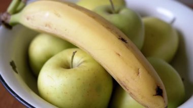 Masasında olgun bir muz olan yeşil elmalı bir kase. Güneş ışığında meyve vitamini seti. Yakın plan. Sağlıklı beslenme.