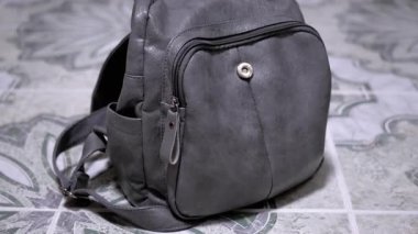 Gri bir sırt çantası fayanslarla kaplı bir zeminde duruyor. Yolculuğa ya da günlük kullanıma hazır. Yaşam tarzı ve seyahat projeleri için harika..