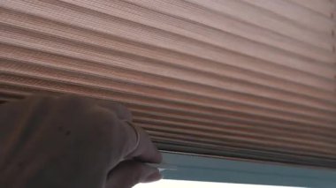 Kadın elleri parlak güneş ışığından dolayı bej kaplamalı pencereleri kapatır. Pencere perdeleri kayıyor. Yakın plan..