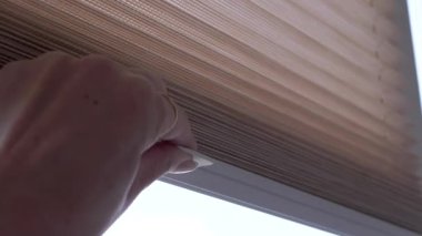 Kadın elleri parlak güneş ışığından dolayı bej kaplamalı pencereleri kapatır. Pencere perdeleri kayıyor. Yakın plan..