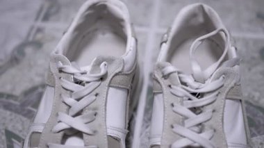 Üstten görünen beyaz spor ayakkabıları ve desenli bir yüzeyde bağcıksız bağcıklar. Gri süet aksanlar biraz stil katıyor. Yaşam tarzı, moda ve e-ticaret için mükemmel..