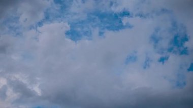 Dramatic time-lapse of dark grey storm clouds quickly forming and moving across a patch of blue sky, showing turbulent formations and birds flying by, heralding an impending weather change.