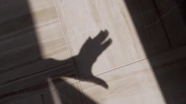 A distinct shadow of a human hand forms a thumbs up gesture, cast dramatically across a light-colored tiled floor by natural sunlight. It conveys approval, success, or positive feedback.