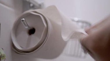 A close-up shot of a hand pulling and tearing off sheets of eco-friendly, recycled toilet paper from a roll in a clean bathroom setting.